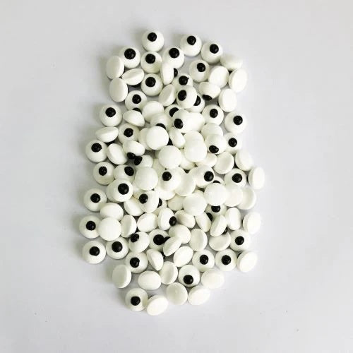 A pile of white candy eyeballs with black pupils, arranged on a plain light gray background.
