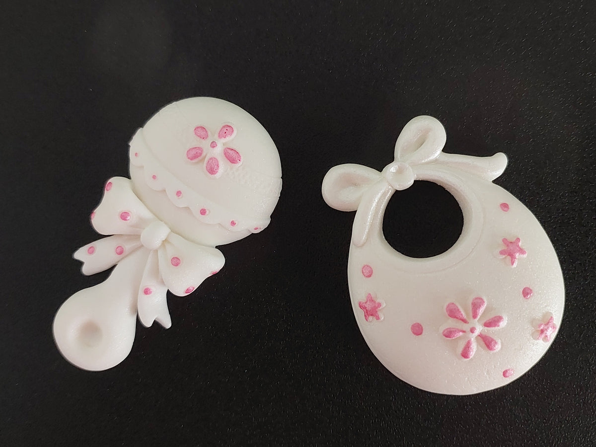 Baby rattle and bib in white and pink. Edible fondant icing cake decorations