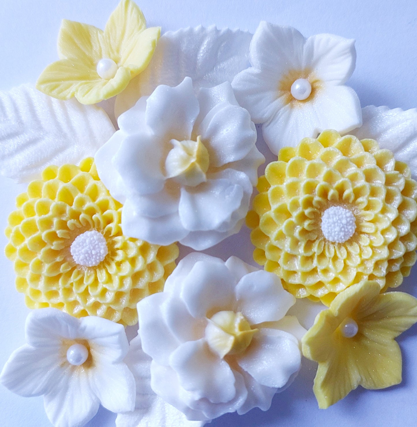 A collection of edible fondant icing flowers and leaves, primarily in yellow and white colors, some decorated with sugar pearls by Cake Candy NZ