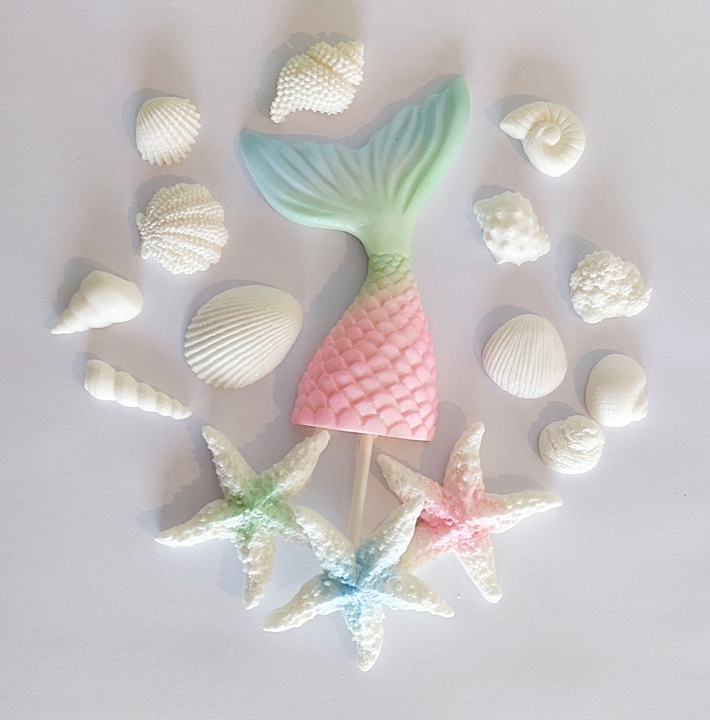A set of edible fondant decorations, featuring a mermaid tail and various shells, arranged on a neutral background.