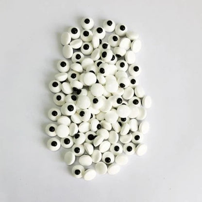 A pile of white candy eyeballs with black pupils, arranged on a plain light gray background.