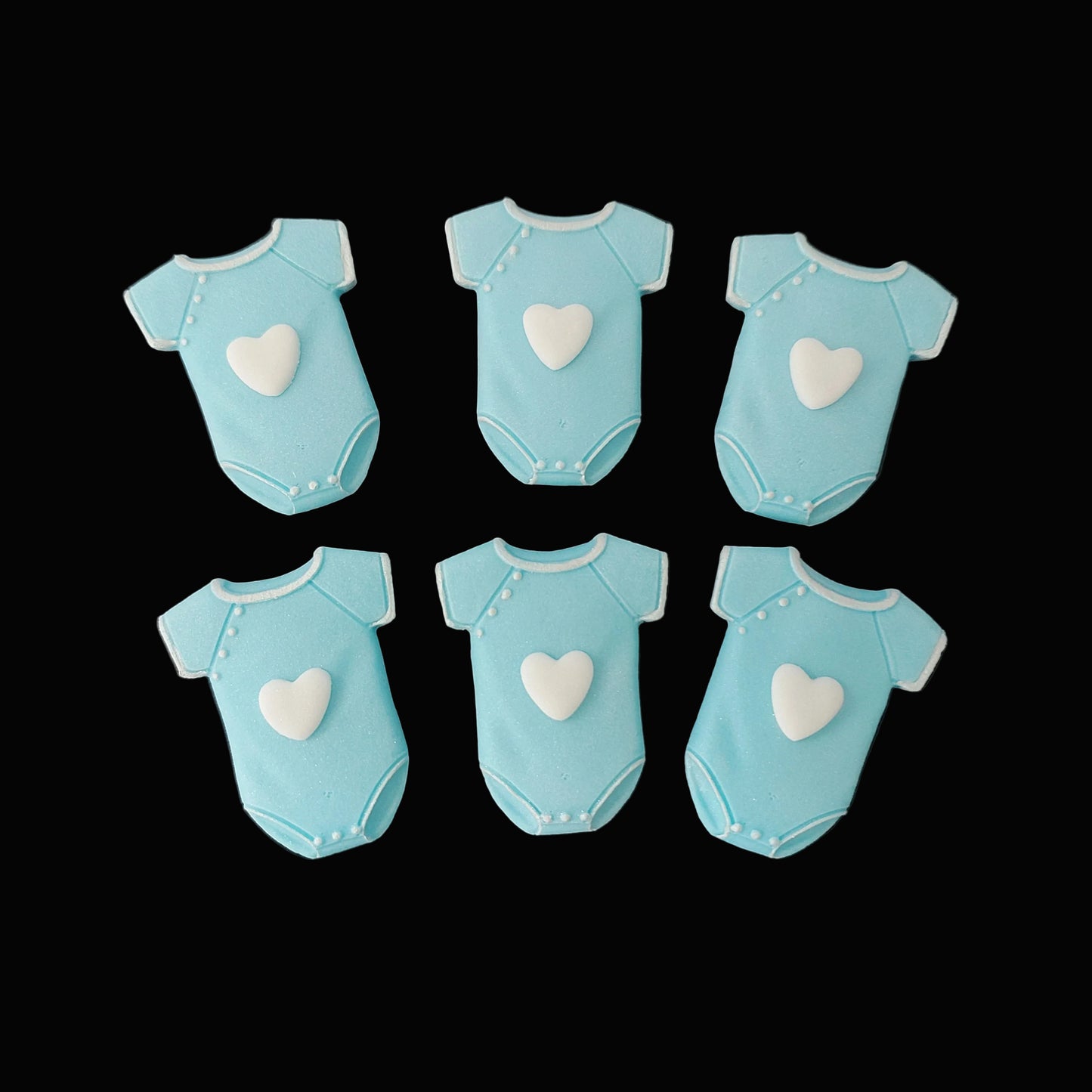 Six blue baby onesies with white hearts on the front, fondant icing cake decorations.