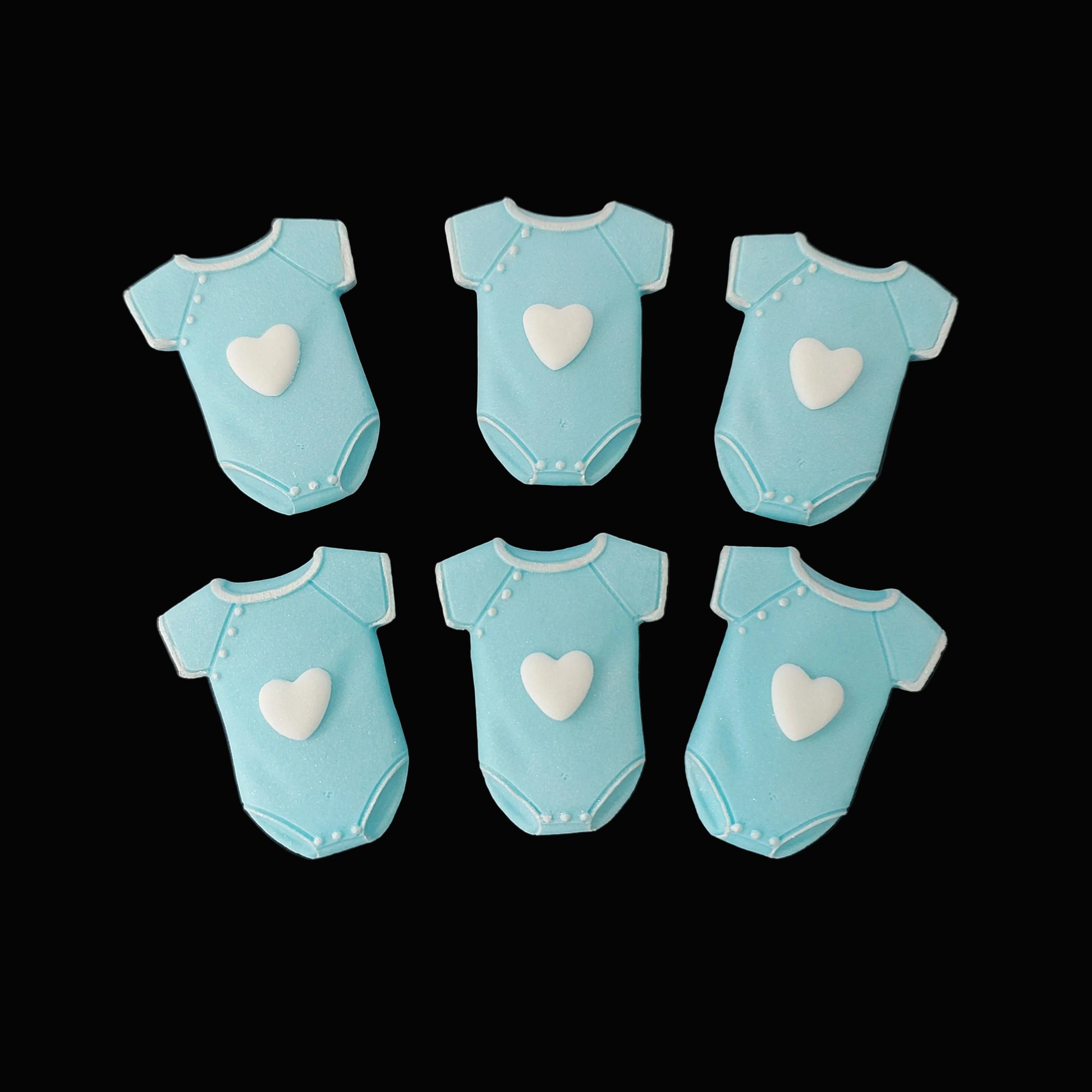 Six blue baby onesies with white hearts on the front, fondant icing cake decorations.