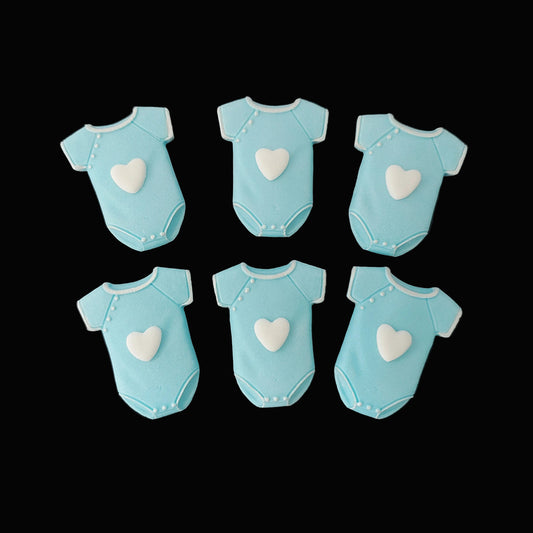 Six blue baby onesies with white hearts on the front, fondant icing cake decorations.