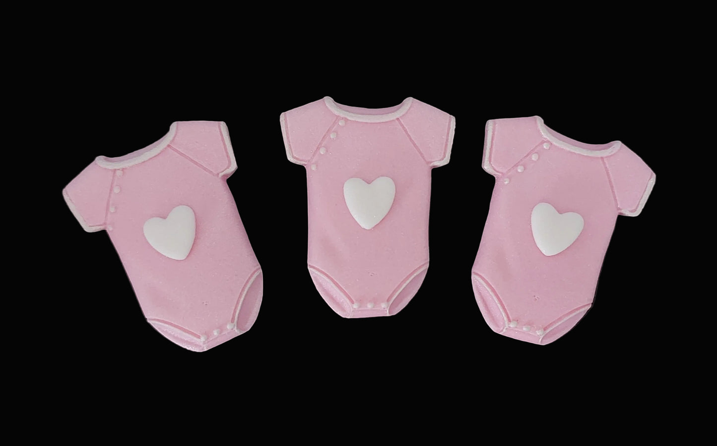 Three pink baby onesies with white hearts on the front, fondant icing cake decorations.