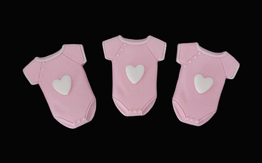 Three pink baby onesies with white hearts on the front, fondant icing cake decorations.