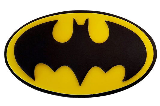 A fondant icing logo resembling the Batman symbol, consisting of a black bat silhouette on a yellow and black background, shaped in an oval. Edible decoration by Cake Candy NZ
