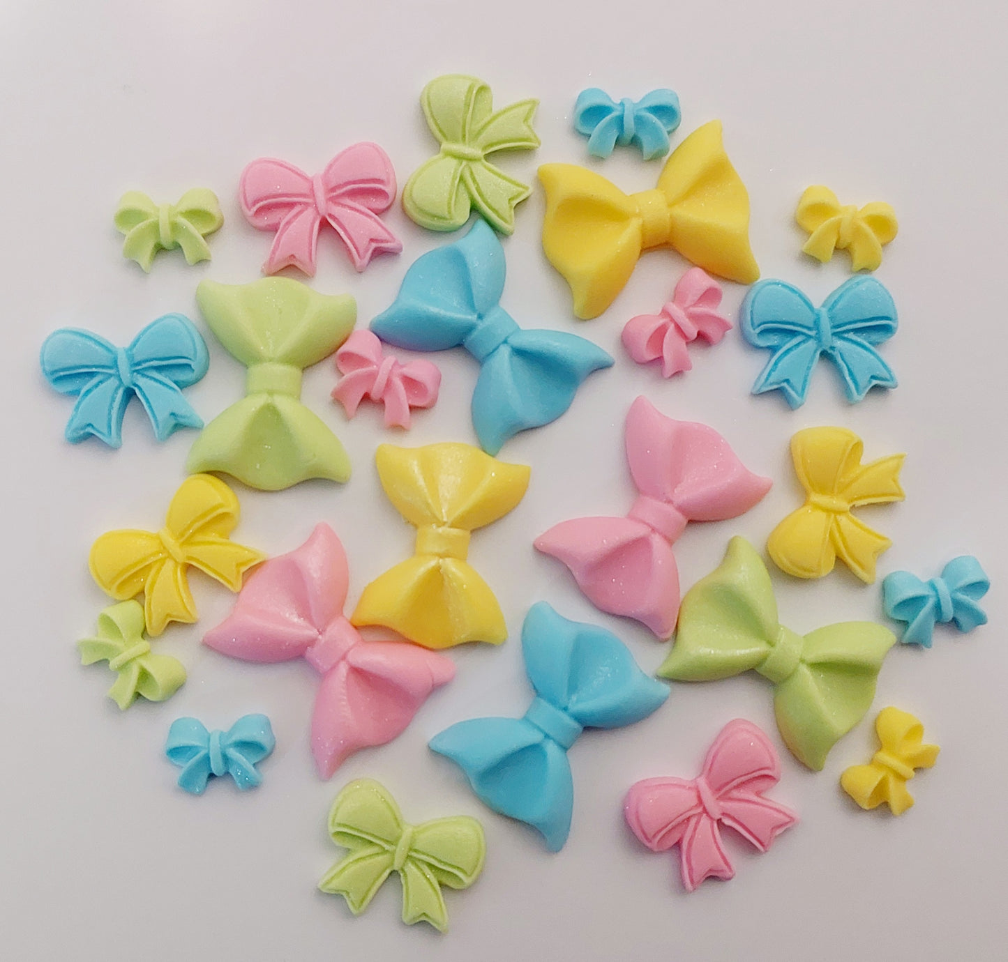 A collection of small, colorful, edible bow-shaped cake decorations.