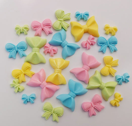 A collection of small, colorful, edible bow-shaped cake decorations.