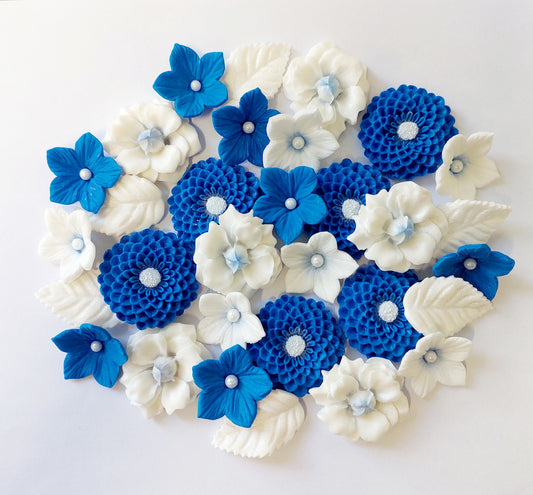 A collection of edible fondant icing flowers and leaves, primarily in blue and white colors, some decorated with sugar pearls by Cake Candy NZ