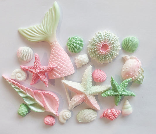 A collection of pink and green colored fondant icing decorations, including mermaid tails and shells, on a white background.
