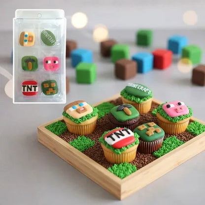 Minecraft-themed cupcake decorations and cupcakes displayed on a wooden tray, with a small inset showing the packaged set. The cupcakes are decorated with pixelated faces, grass, dirt, and block motifs including TNT, a creeper, a pig, and a Minecraft sign.