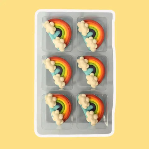 Six rainbow with clouds-shaped with cloud cake decorations in a clear plastic mold on a yellow background