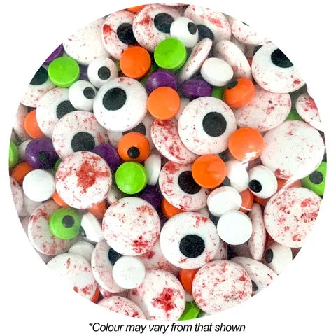 A circular close-up of assorted Halloween candy sprinkle eyeballs in white, orange, green, purple, and red splatter, with small black centers. Text below reads '*Colour may vary from that shown' on a white background.