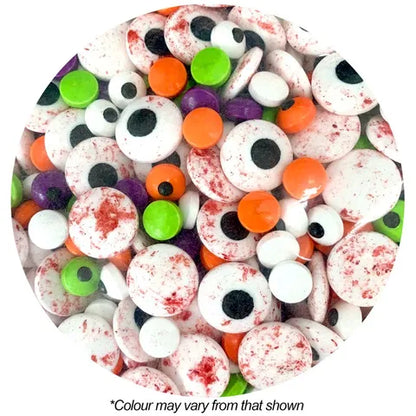 A circular close-up of assorted Halloween candy sprinkle eyeballs in white, orange, green, purple, and red splatter, with small black centers. Text below reads '*Colour may vary from that shown' on a white background.