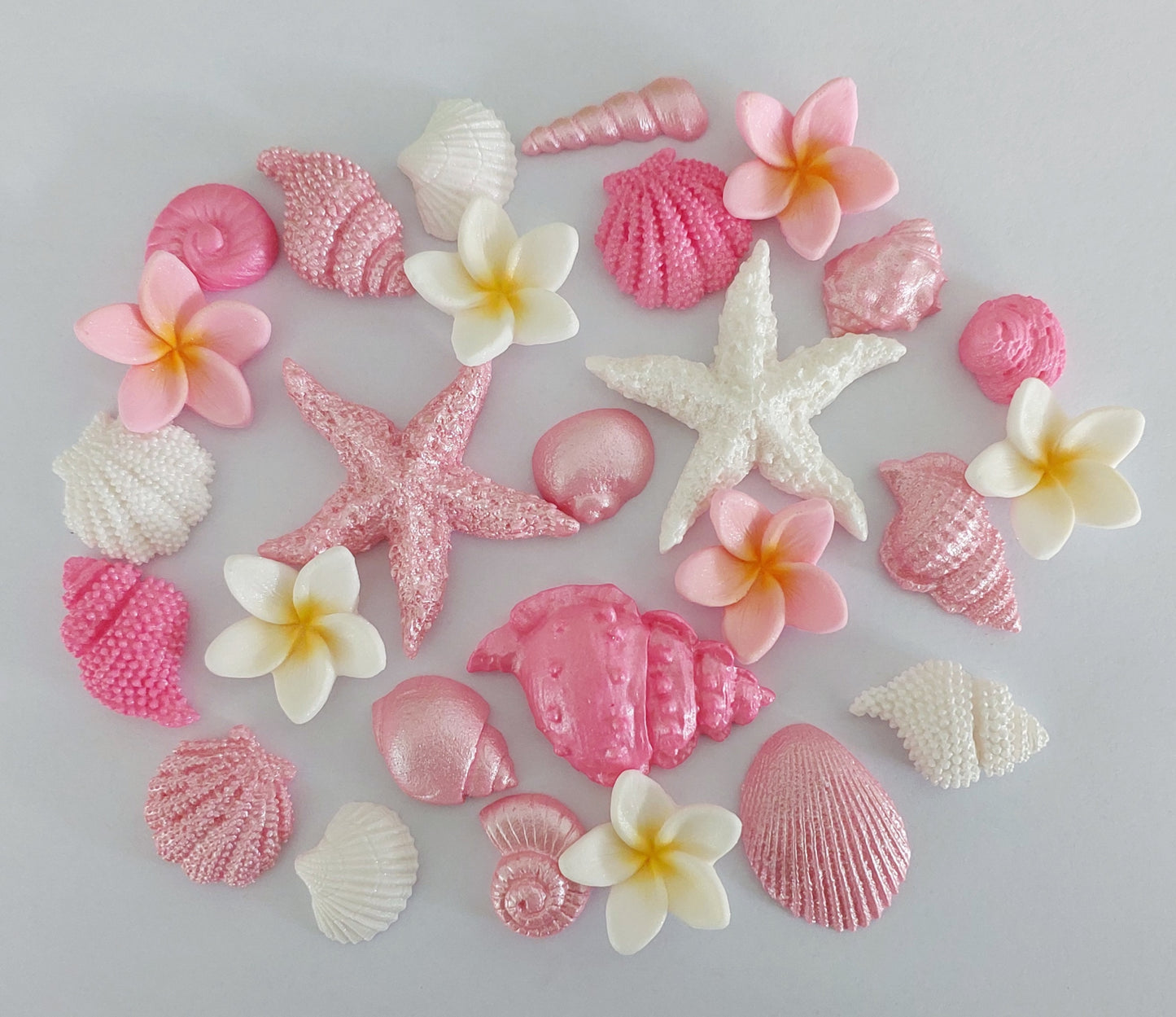 A collection of fondant edible decorations shaped like shells, starfish and tropical flowers, primarily in pink and white shades.
