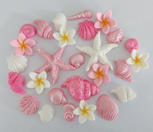 A collection of fondant edible decorations shaped like shells, starfish and tropical flowers, primarily in pink and white shades.