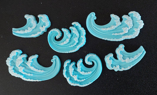 A set of six blue fondant icing decorations shaped like waves, with a sparkle on each, displayed on a black background.